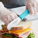 A person using a Choice stainless steel sandwich spreader to cut a sandwich.