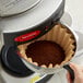 A hand pouring Crown Beverages Emperor's Blend Decaf coffee into a coffee filter.