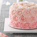 A white square melamine-coated wood cake board with a cake with pink frosting and roses on top.