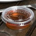 A Solo clear plastic souffle lid on a plastic cup with brown liquid next to a knife.