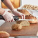 A person using an Avantco electric knife to cut a loaf of bread.