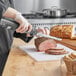 A person cutting meat on a cutting board with an Avantco cordless electric knife.
