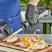 A person in black gloves uses a Backyard Pro cordless electric knife to cut up chicken on a cutting board.