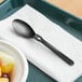 A black WeGo spoon on a napkin next to a bowl of fruit.