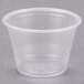 A Dart clear plastic souffle cup with a lid on a grey surface.