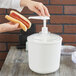 A woman using a Carlisle white condiment pump to dispense hot dog toppings.