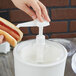 A person using a Carlisle white insulated condiment pump to put ketchup on a hot dog.