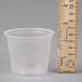 A Dart clear plastic souffle cup on a grey surface with a ruler.