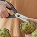 A person cutting an artichoke with Choice stainless steel kitchen shears.