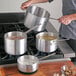 A person using a Choice aluminum sauce pan on a stove with other pots.