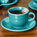 A turquoise Fiesta saucer with a tea cup and tea bag on it.