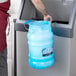 A person's hand using a San Jamar Saf-T-Ice blue ice tote to fill a large ice container.