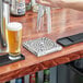 A hand holding a glass of beer over a stainless steel beer drip tray.