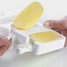 A person using a Silikomart Classic Ice Cream Silicone Baking Mold to make a yellow ice cream bar on a popsicle stick.