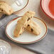 A close up of an Acopa Keystone vanilla bean stoneware coupe plate with two cookies.