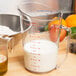A Cambro clear polycarbonate measuring cup on a table with milk in it.
