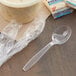 A Visions individually wrapped clear plastic soup spoon on a table with other wrapped plastic spoons.