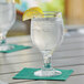 An Acopa glass goblet of water with a lemon wedge on a table