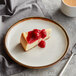 A slice of cheesecake with cherry sauce on an Acopa Keystone vanilla bean stoneware coupe plate.
