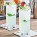 Two Acopa beverage glasses with ice, lime slices, and a leaf on a table.