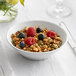 A bright white Acopa Liana porcelain bowl filled with granola and berries.