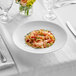 A white Acopa Liana porcelain pasta bowl filled with pasta, shrimp, and herbs.