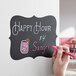 A person's hand writing "Happy Hour" in red on a Choice decorative chalkboard label.