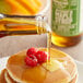 A close-up of Butternut Mountain Farm Grade A Amber Pure Vermont Maple Syrup being poured onto pancakes with raspberries.
