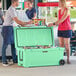 A man and woman standing next to a CaterGator Seafoam outdoor cooler with the lid open.