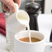 A person using a white American Metalcraft porcelain creamer to pour milk into a cup of coffee.