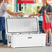A man and woman standing next to a white CaterGator outdoor cooler with the lid open.