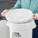 A person holding a white lid on a white bucket filled with ice.