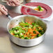 A person using a Vollrath saute pan to stir vegetables on a table.