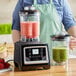 A woman in an apron uses an AvaMix commercial blender to make a green smoothie.