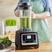 A woman in an apron using an AvaMix commercial blender to make a green smoothie.