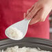 A person holding an Avantco 7" rice paddle spoonful of rice over a bowl of rice.