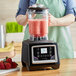 A woman in a green apron using an AvaMix commercial blender to make a smoothie.