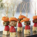 Bamboo skewers with heart-shaped ends holding cheese, tomatoes, and orange food items.