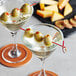 Two martini glasses with Bamboo by EcoChoice red bamboo knot skewers holding olives on a table.