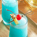 A table with two glasses of blue drinks, each with a pineapple and cherry, with a red bamboo heart skewer in each glass.