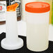 A Carlisle white plastic container with an orange lid and cap next to a white container with a white liquid in it.