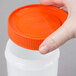 A hand holding an orange lid over a white plastic container with an orange spout