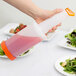 A hand pouring pink liquid from a Carlisle Store 'N Pour container onto a plate of salad.