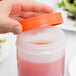 A hand holding a Carlisle white plastic container with a red liquid and an orange spout and cap.