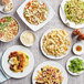 A table with plates of pasta, salad, and other foods, including bowls of Barilla Fettuccine with bacon and vegetables.