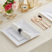 A white table set with Visions rose white plastic plates and classic rolled flatware.