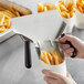 A hand using a Choice stainless steel french fry scoop to fill a white container with french fries.