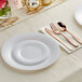 A white Visions plastic dinner plate with silver and gold flatware on a table.