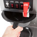 A hand uses a black handle to push the red button on a Bloomfield commercial coffee maker.