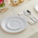 A Visions white plastic dinner plate with silver classic flatware on a white napkin.